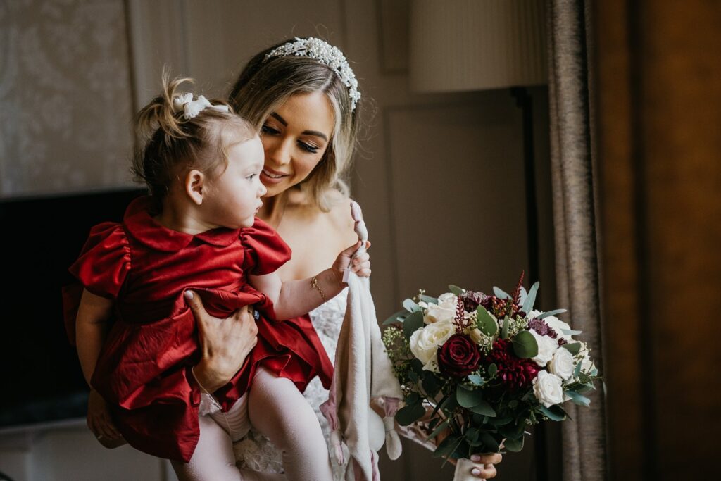 Wedding photo in Ireland of a Bride with a beautiful baby Flower girl, in a striking red dress.
