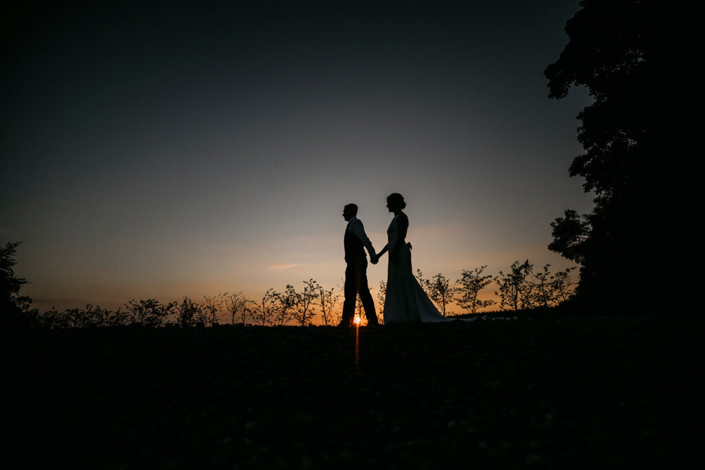 The Wedding couple (Orlaith and Matthew) walking hand in hand at sunset in silhouette.