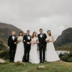 Bride and groom with their bridesmaids and groomsmen on a hillside with mountains behind them