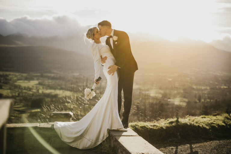 Bride and groom kissing at golden hour with scenic mountain backdrop.
