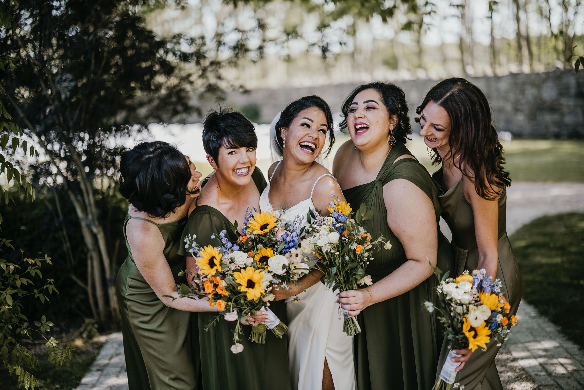Bride and bridesmaids laugh together holding sunflower bouquets