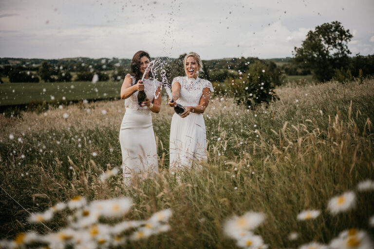 Two brides in a meadow spraying champagne. two brides wedding portraits ireland