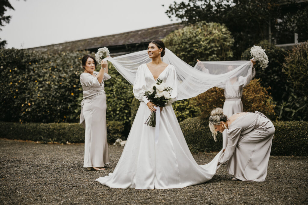 Bride outside with bridesmaids fixing her veil and dress
