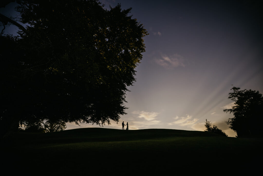 Bride and groom silhouetted on a hill at sunset with dramatic sky during an outdoor wedding portrait in Ireland